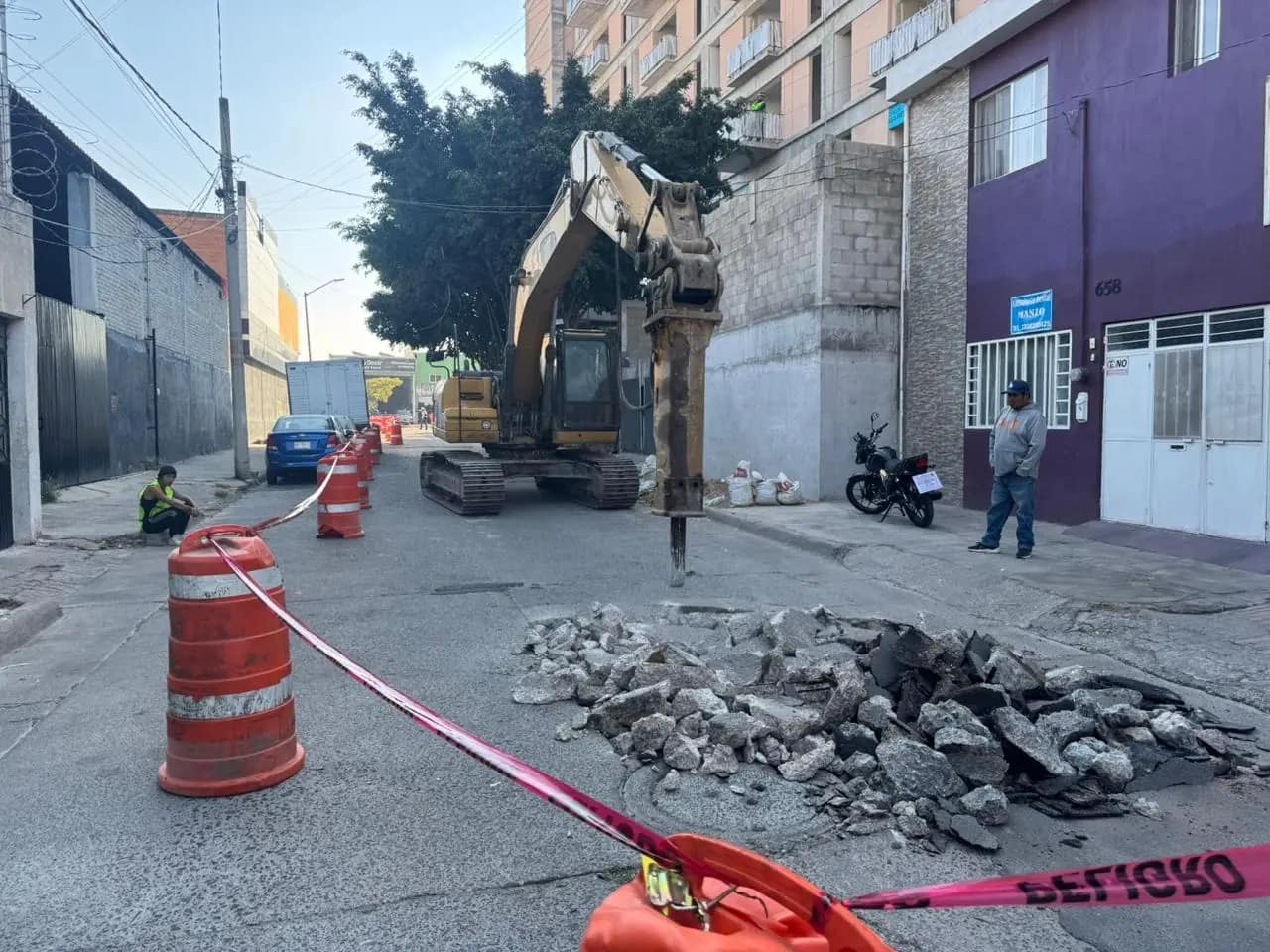 Excavadora con martillo rompiendo pavimento en calle angosta