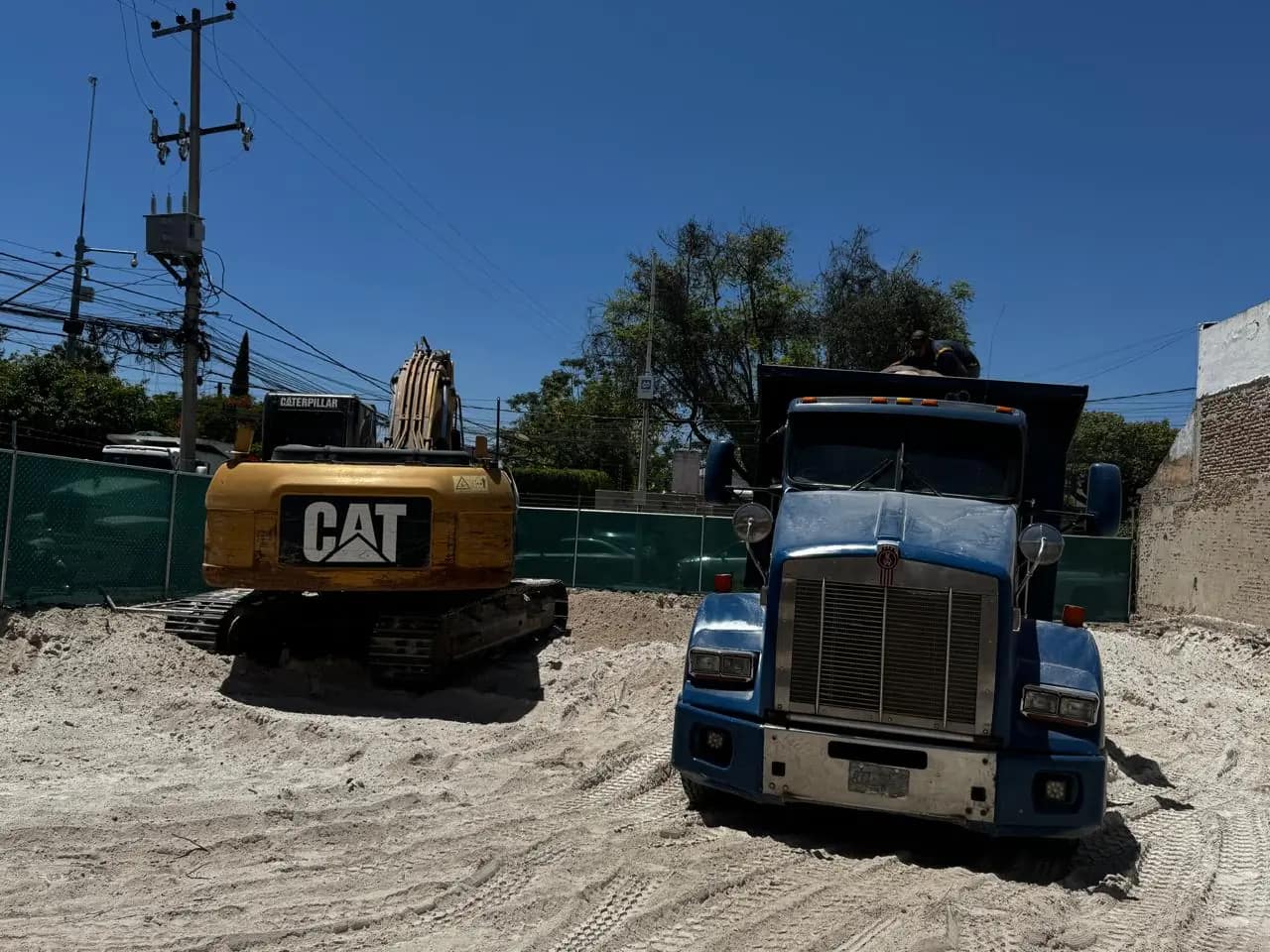 Excavadora CAT y camión de volteo en lote urbano